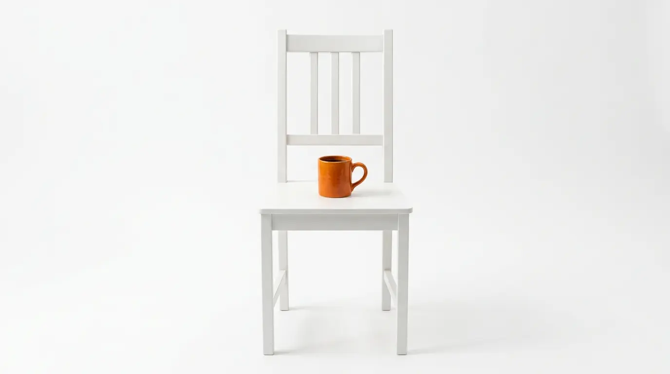 Ein weißer Holzstuhl mit einer orangefarbenen Tasse auf der Sitzfläche steht vor weißem Hintergrund