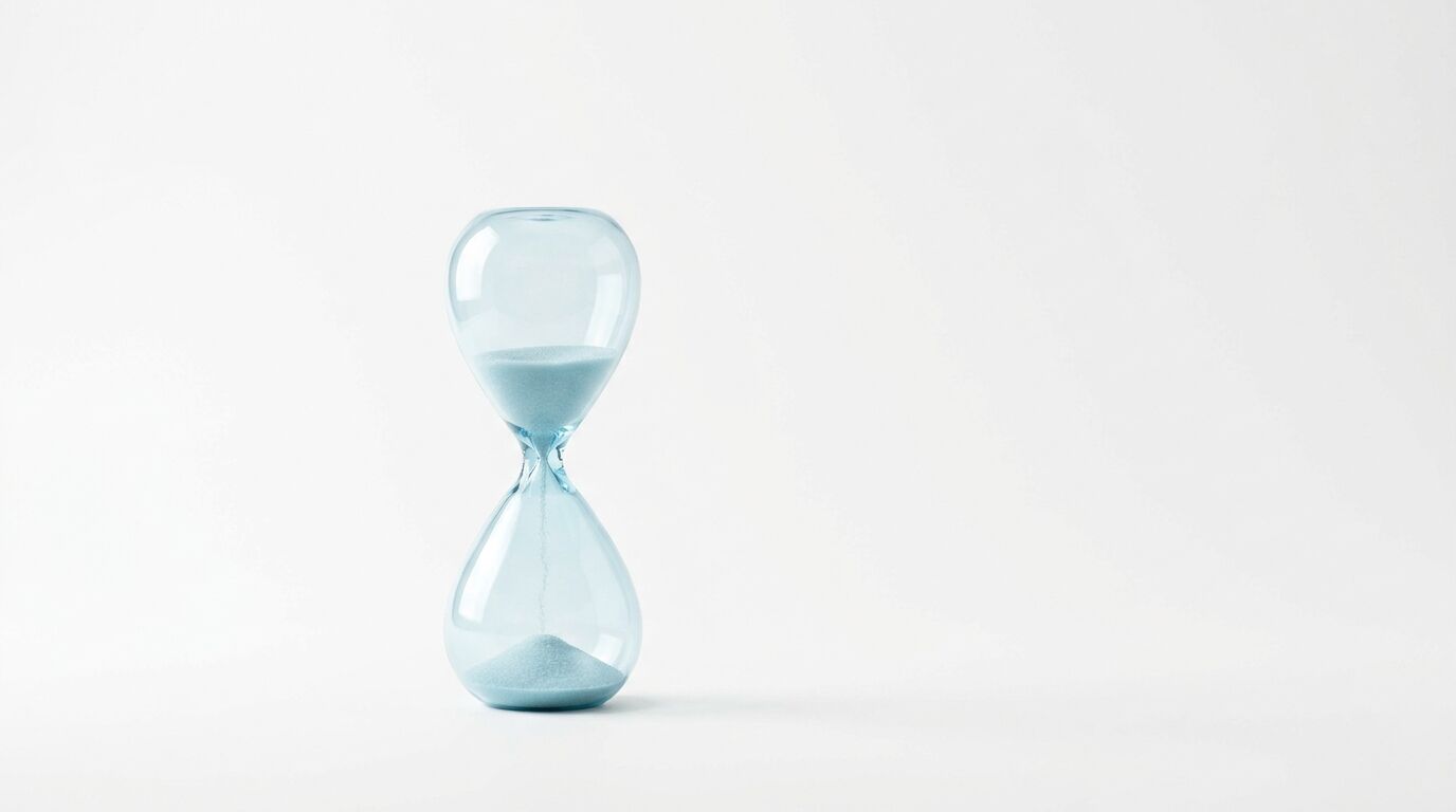 Glas-Sanduhr mit hellblauem Sand vor weißem Hintergrund