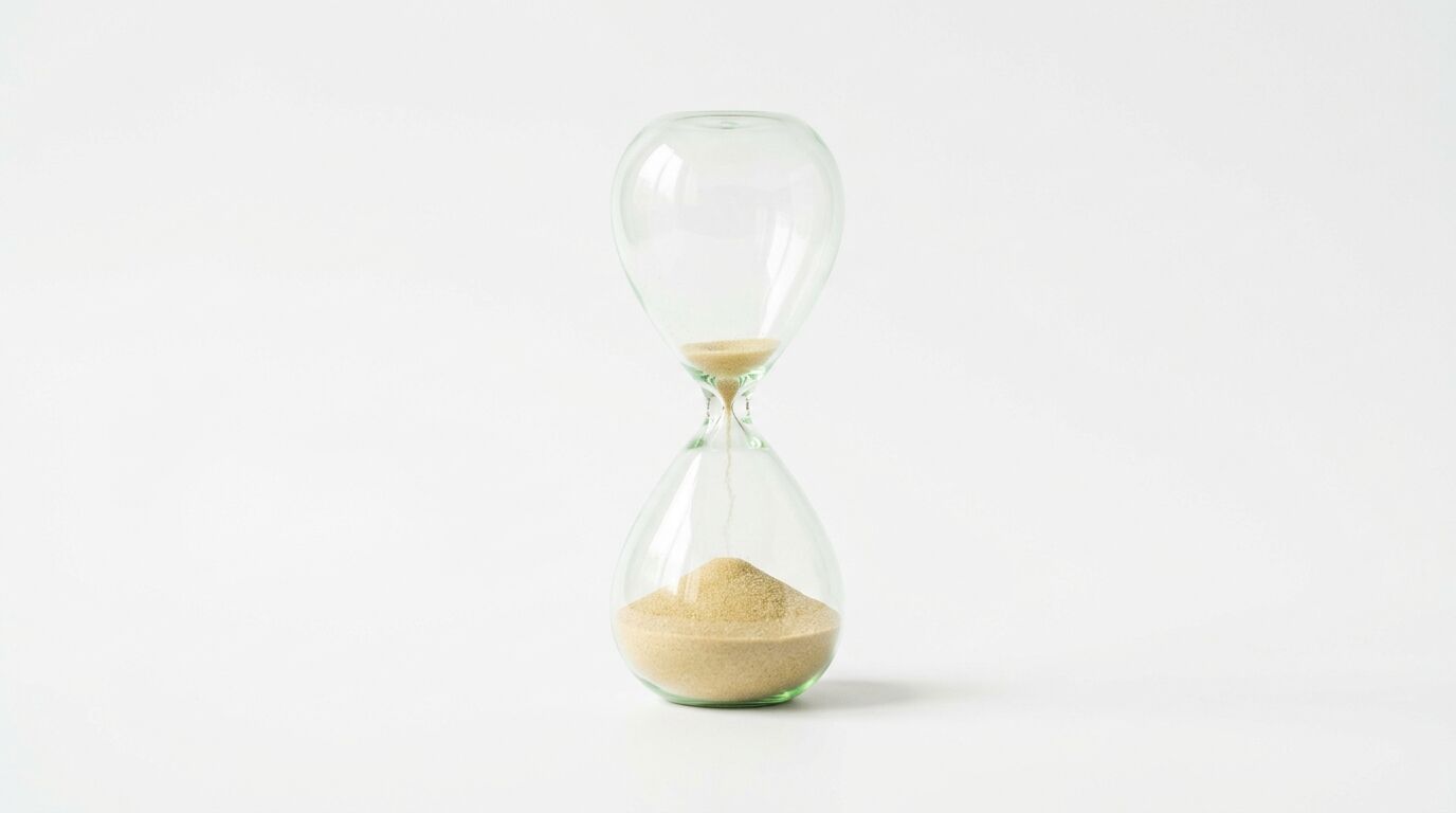 Eine gläserne Sanduhr mit hellem Sand steht zentral vor einem weißen Hintergrund