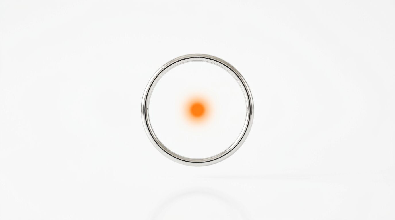 Ein metallischer Ring mit einem diffusen, orangefarbenen Punkt in der Mitte auf weißem Grund