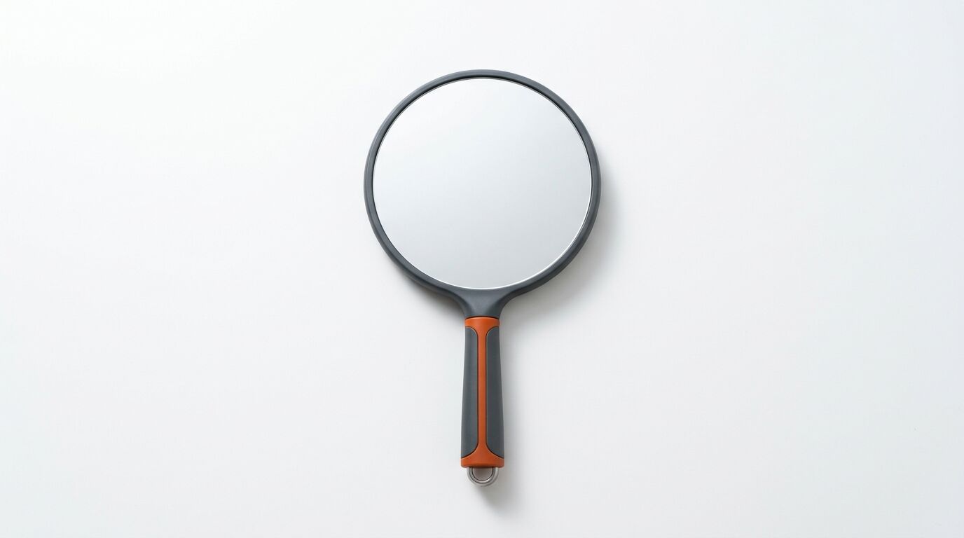 Ein runder Handspiegel mit grau-orangem Griff vor weißem Hintergrund