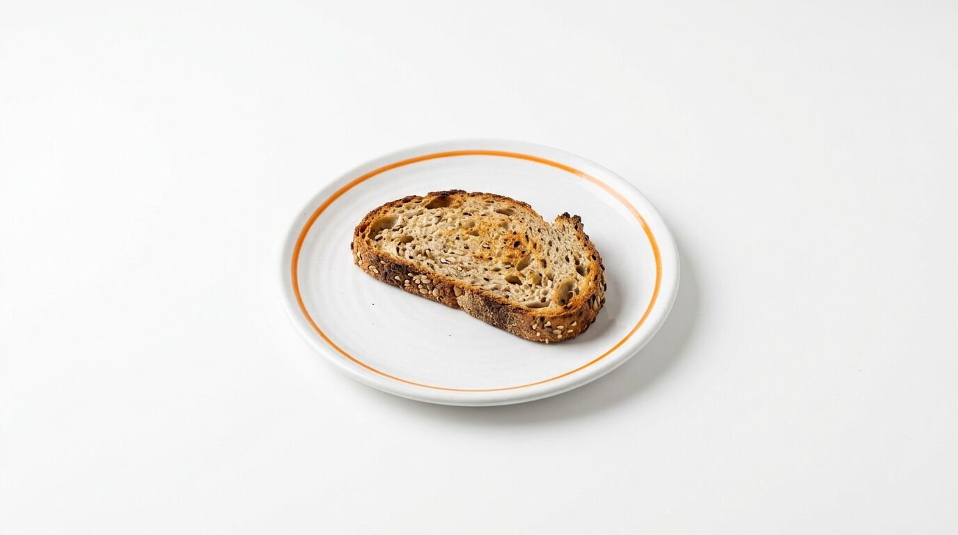Eine geröstete Scheibe Körnerbrot liegt auf einem weißen Teller mit orangefarbenem Rand
