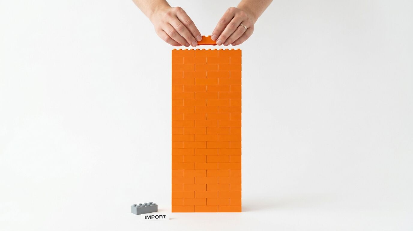 Hände setzen einen Stein auf eine orange Mauer aus Klemmbausteinen vor weißem Hintergrund