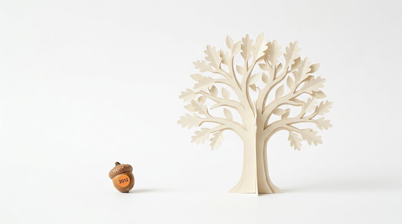 Eine Eichel mit der Aufschrift „2012“ steht links neben einem großen Baum aus Papier auf weißem Grund