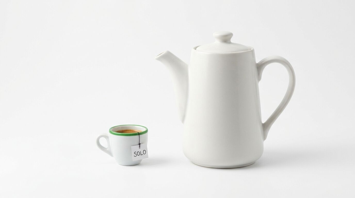Eine weiße Kaffeekanne steht rechts neben einer kleinen weißen Tasse mit Kaffee auf weißem Hintergrund