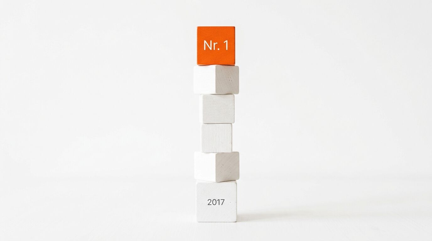 Turm aus Holzklötzen vor weißem Hintergrund. Oben oranger Klotz mit „Nr. 1“, unten weiß mit „2017“