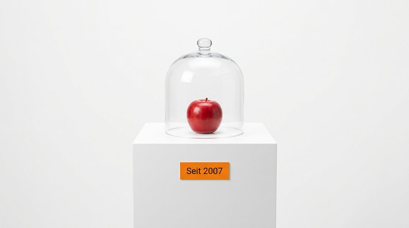 Apfel unter Glassturz auf Sockel mit Plakette vor weißem Hintergrund