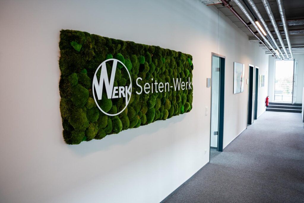 Logo und Schriftzug von Seiten-Werk auf einer Mooswand im Flur der Agentur